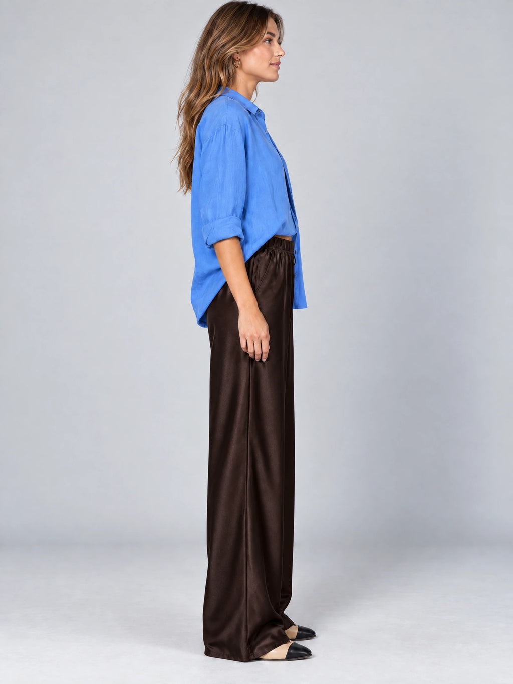 Side studio view of a model wearing Brown satin wide leg pants with a high elastic waist.