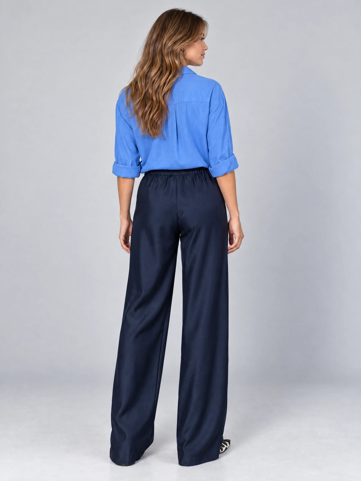 Back studio view of a model wearing Navy satin wide leg pants with an elastic high waist.