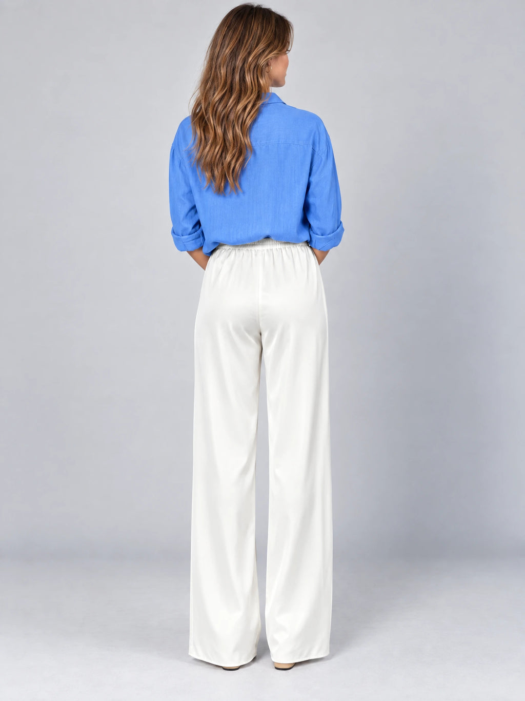 Back view of a model wearing White satin wide leg pants with a high gathered waist in a studio.