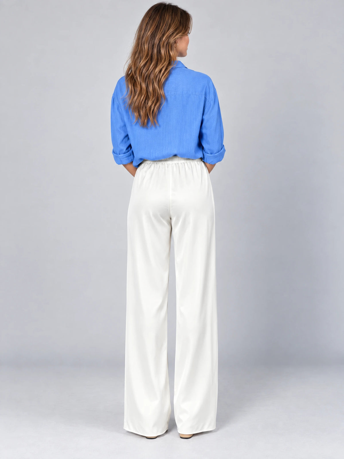 Back view of a model wearing White satin wide leg pants with a high gathered waist in a studio.