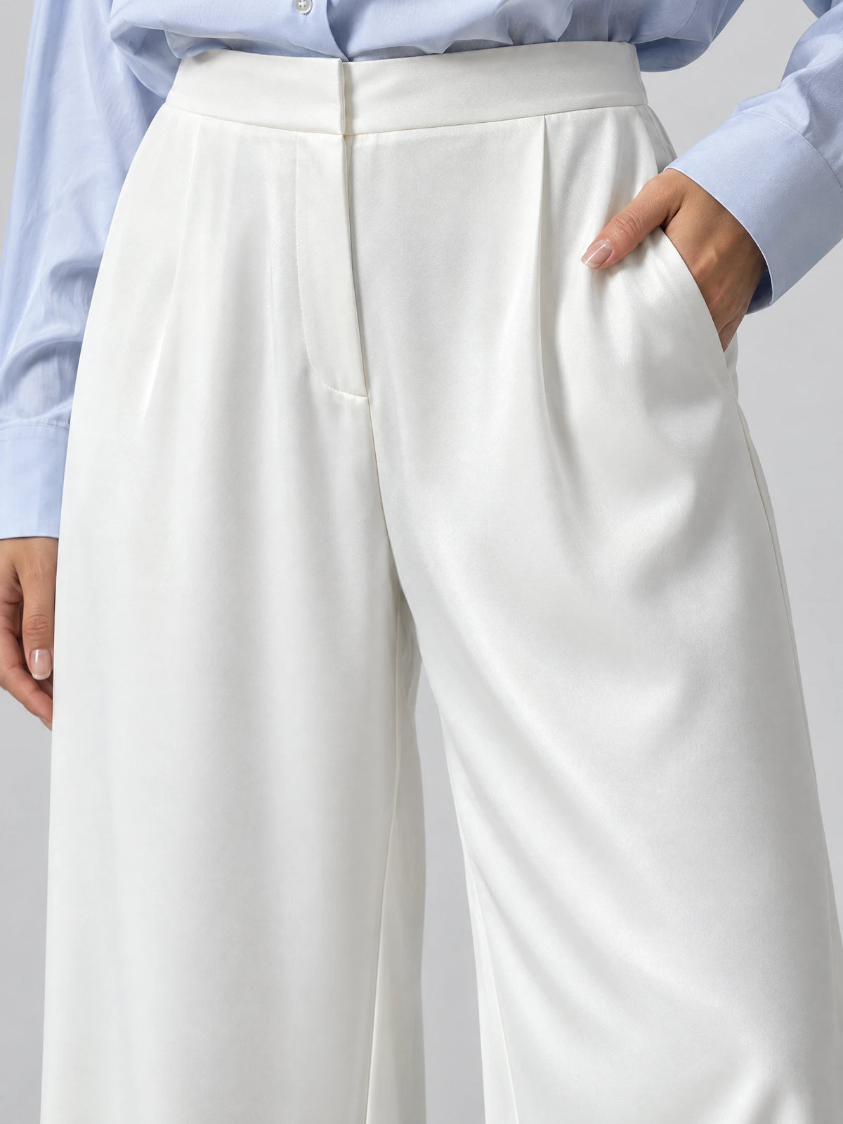 Close-up of White satin wide leg pants showing the high waistband, front pleats, and side pocket.