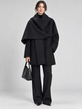 Front studio view of a model wearing a Black scarf collar wool coat with an oversized draped collar and side pockets.