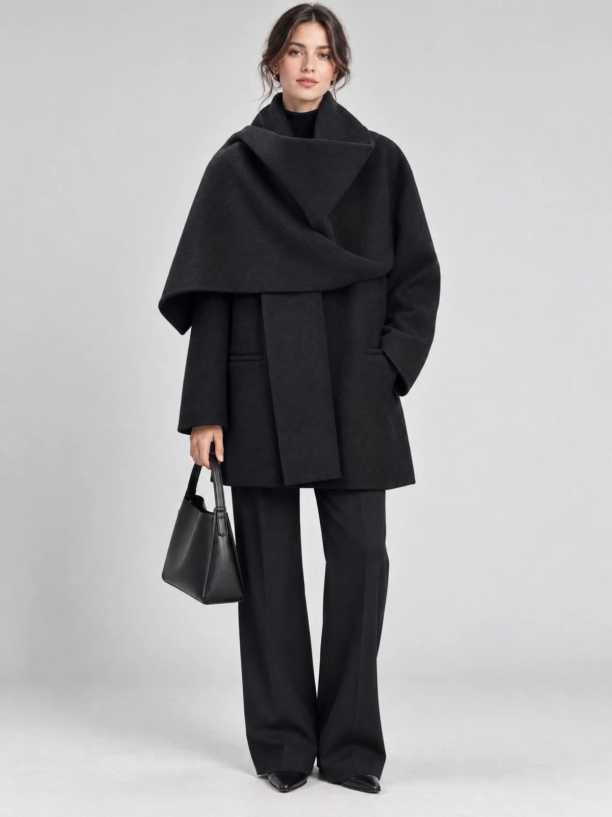 Front studio view of a model wearing a Black scarf collar wool coat with an oversized draped collar and side pockets.