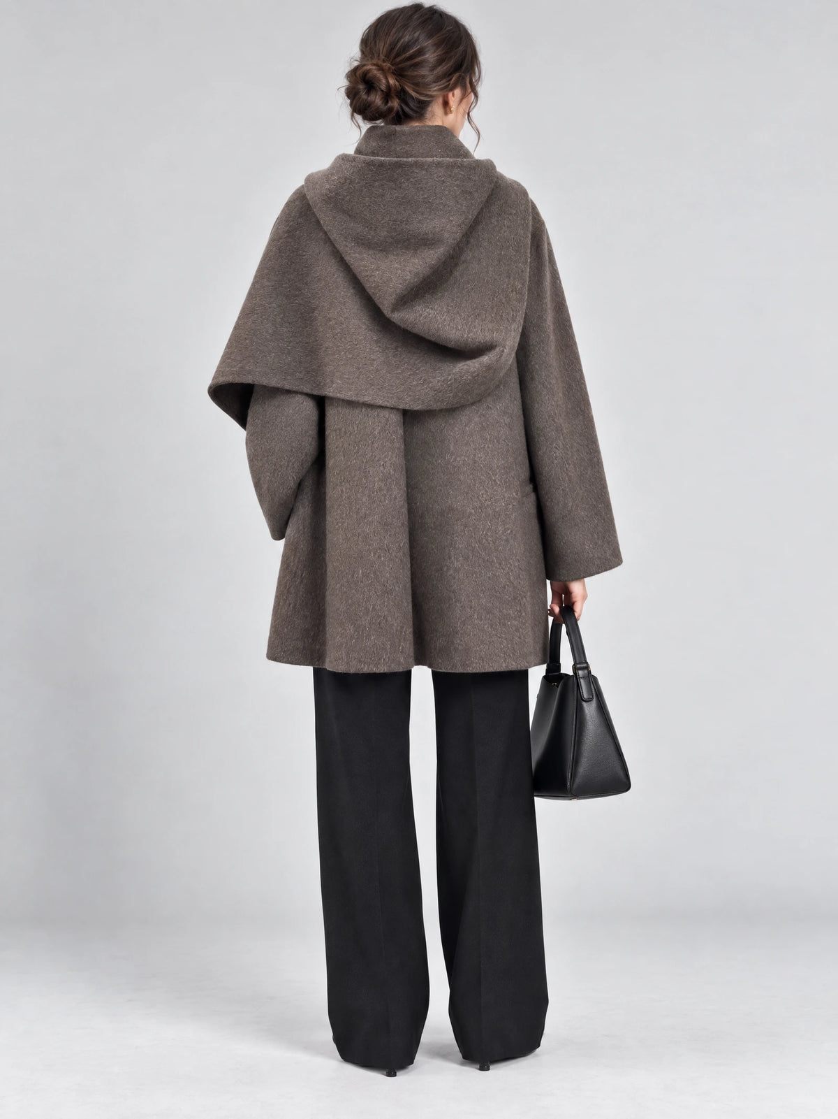 Rear studio view of a model wearing a Brown wool coat with a draped scarf collar and wide sleeves.