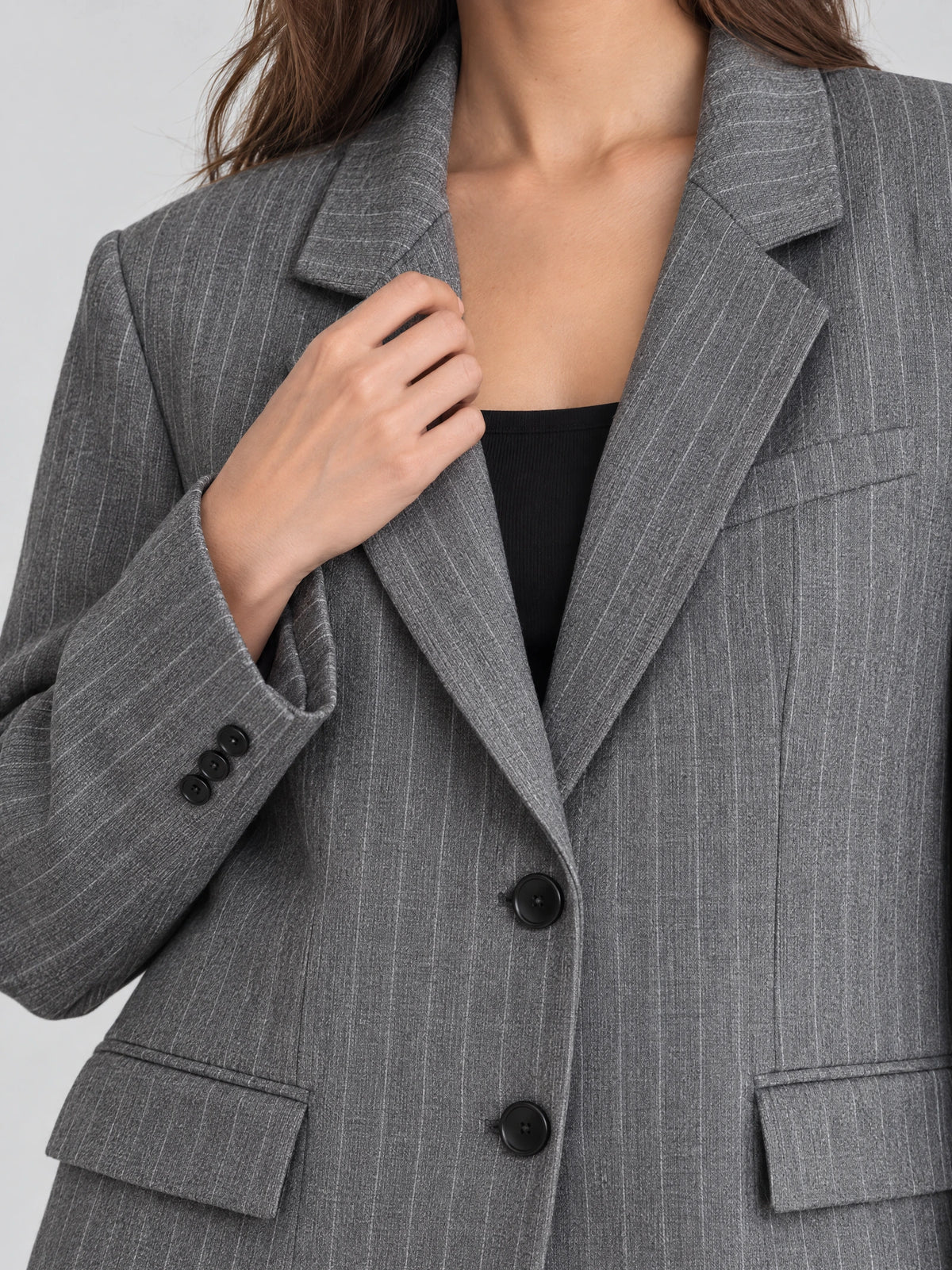 Close-up of a Gray striped single breasted blazer showing the notched lapels, front buttons, flap pockets, and buttoned cuff.