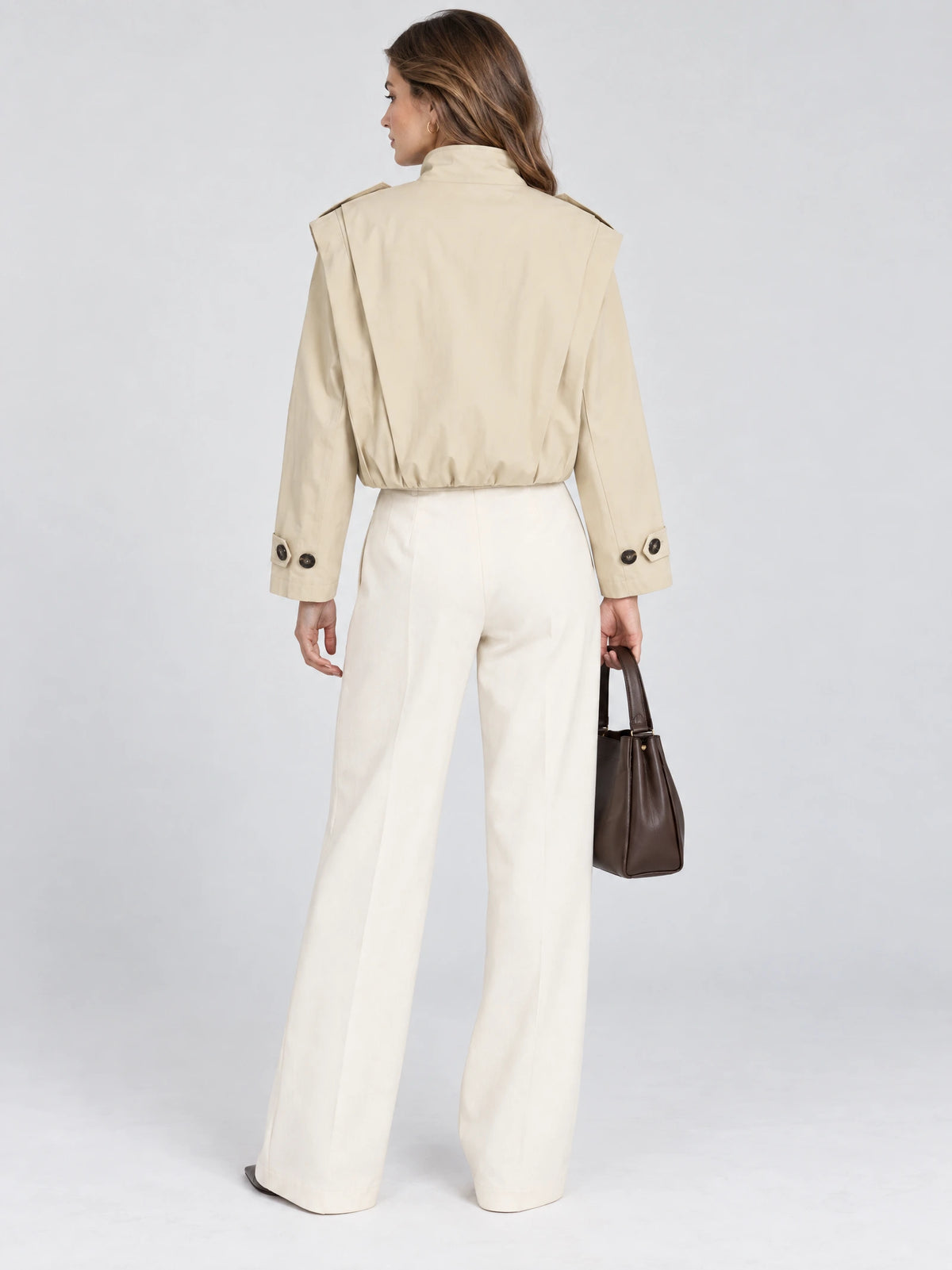 Rear view of a model wearing a Khaki cropped stand-collar trench coat with shoulder tabs and buttoned cuffs.