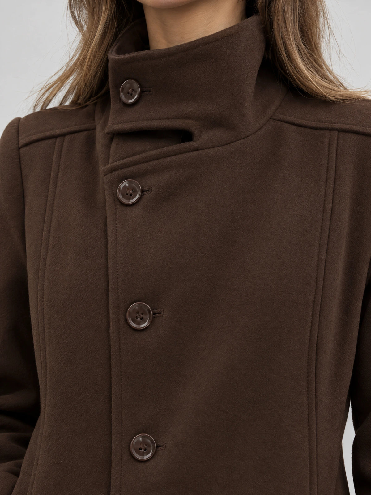 Close-up of a Brown womens turtleneck coat with a high stand collar, button front, and stitched panel detailing.
