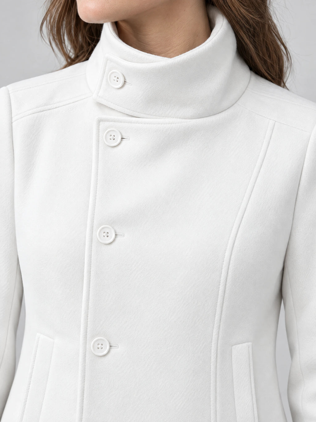 Close-up of a White womens turtleneck coat with a high button-tab collar, covered placket, and vertical welt pockets.