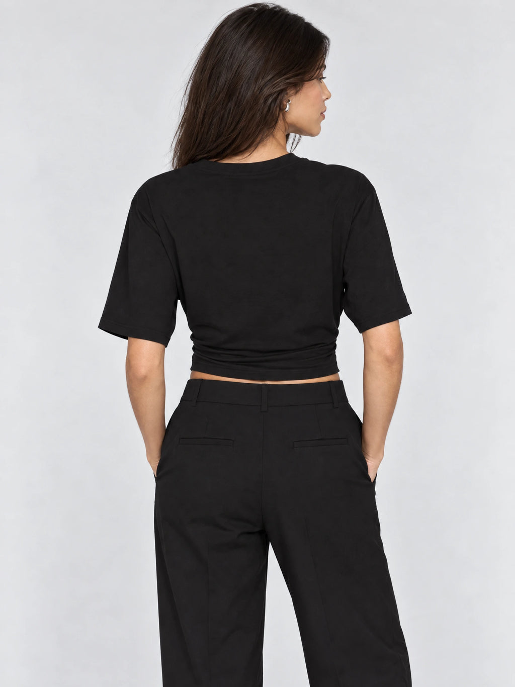 Back view of model wearing a Black cotton waist short top with short sleeves and a fitted cropped hem.