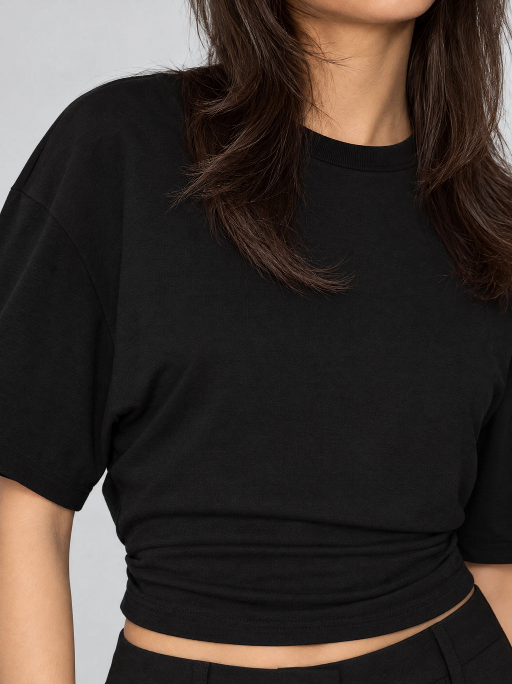 Close-up of the Black cotton Waist Short Top, showing its ribbed crew neckline, dropped shoulder seam, and gathered cropped hem.