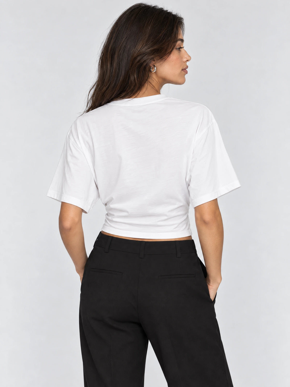 Back view of a model wearing a White cotton waist short top with short sleeves and a fitted hem.