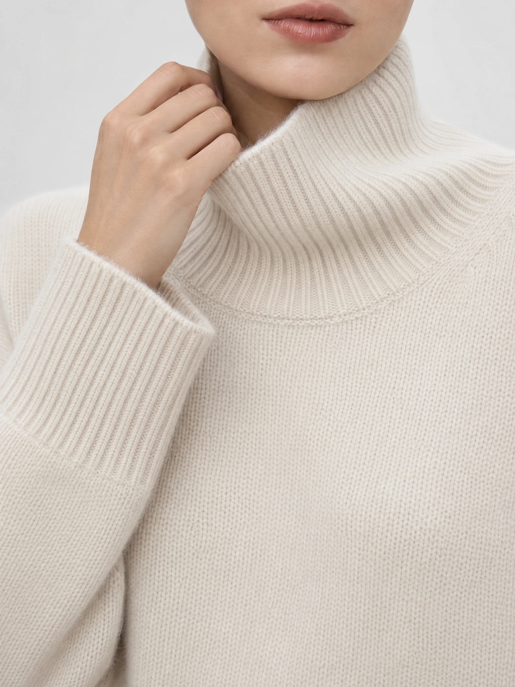 Close-up of a Beige women’s turtleneck sweater showing the ribbed fold-over collar, knit texture, and ribbed cuff.