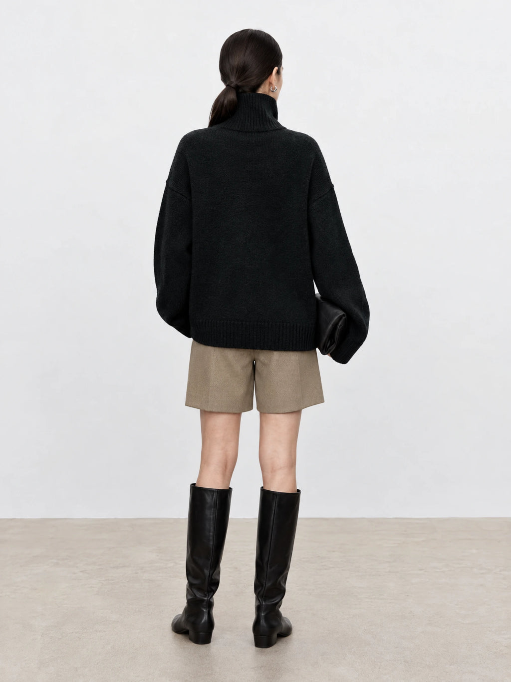 Rear studio view of a model wearing a Black wool turtleneck sweater with a ribbed high neck, relaxed sleeves, and ribbed hem.
