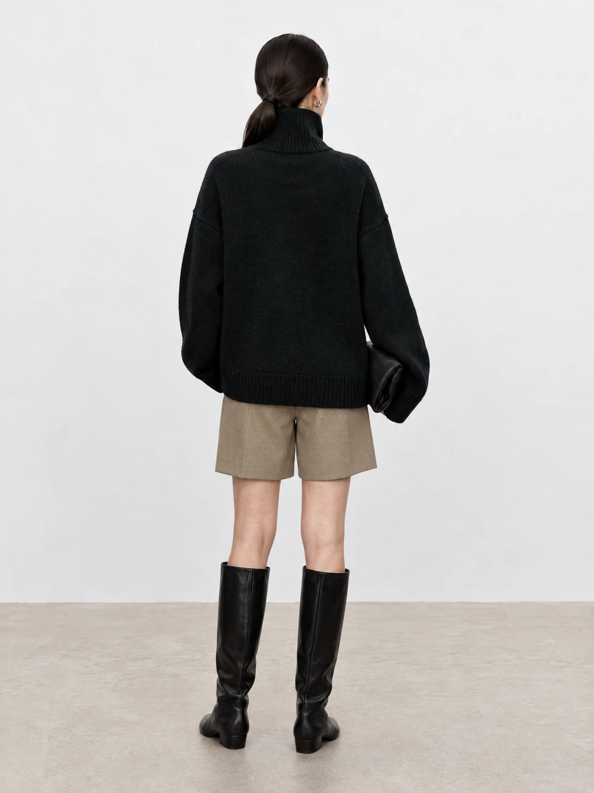 Rear studio view of a model wearing a Black wool turtleneck sweater with a ribbed high neck, relaxed sleeves, and ribbed hem.