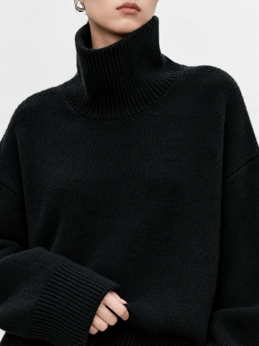 Close-up of a Black women’s turtleneck sweater showing its ribbed high collar, textured knit, and wide ribbed cuffs.
