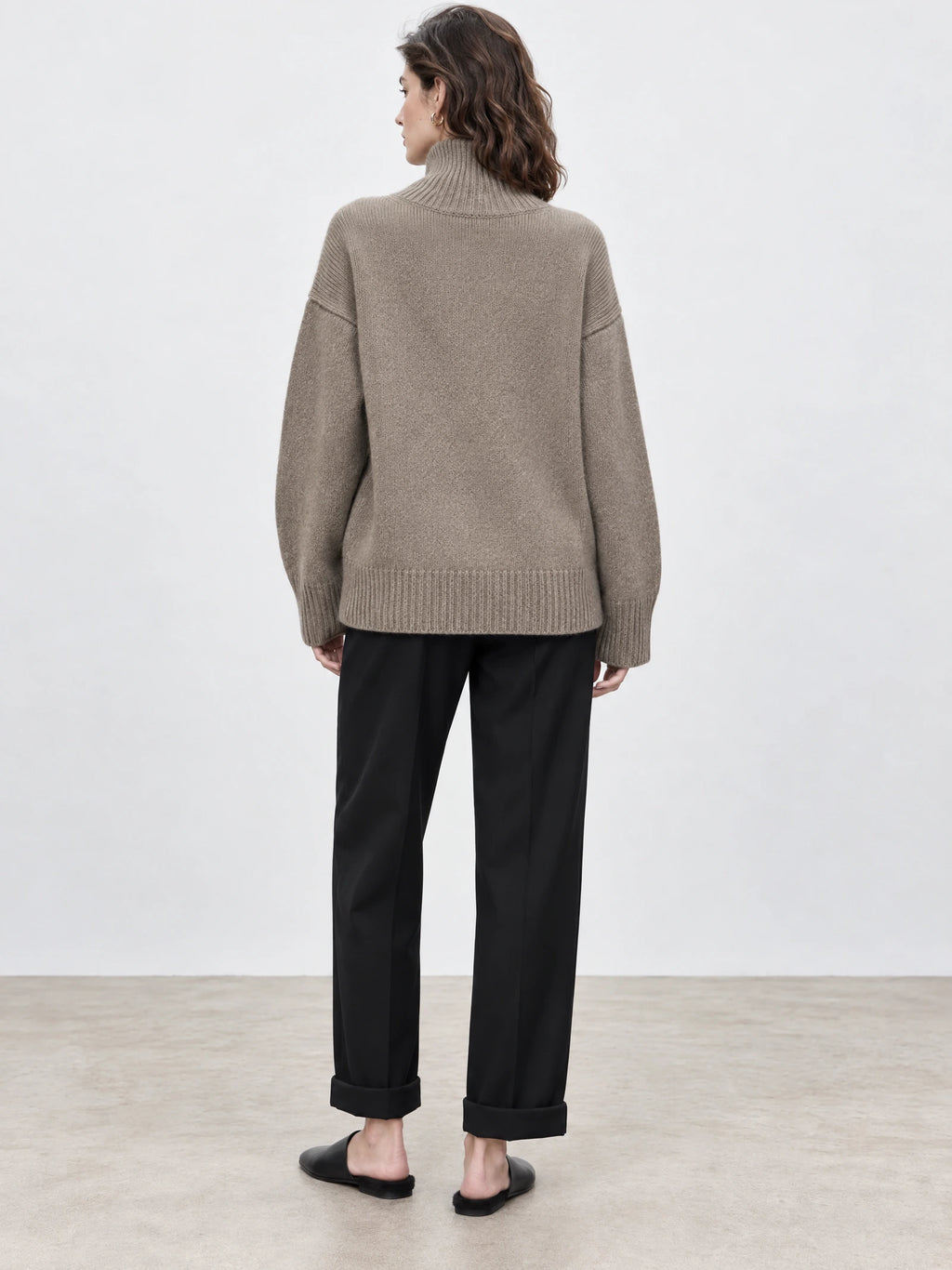 Back view of a model wearing a Khaki wool turtleneck sweater with a ribbed high neck, cuffs, and hem.