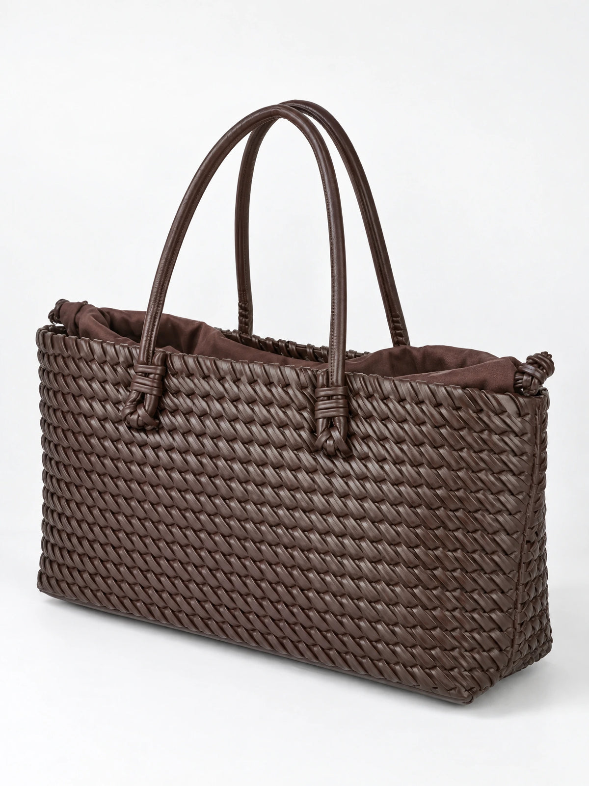 Brown woven shoulder bag shown at an angle with braided texture, knotted handles, and a gathered lining.