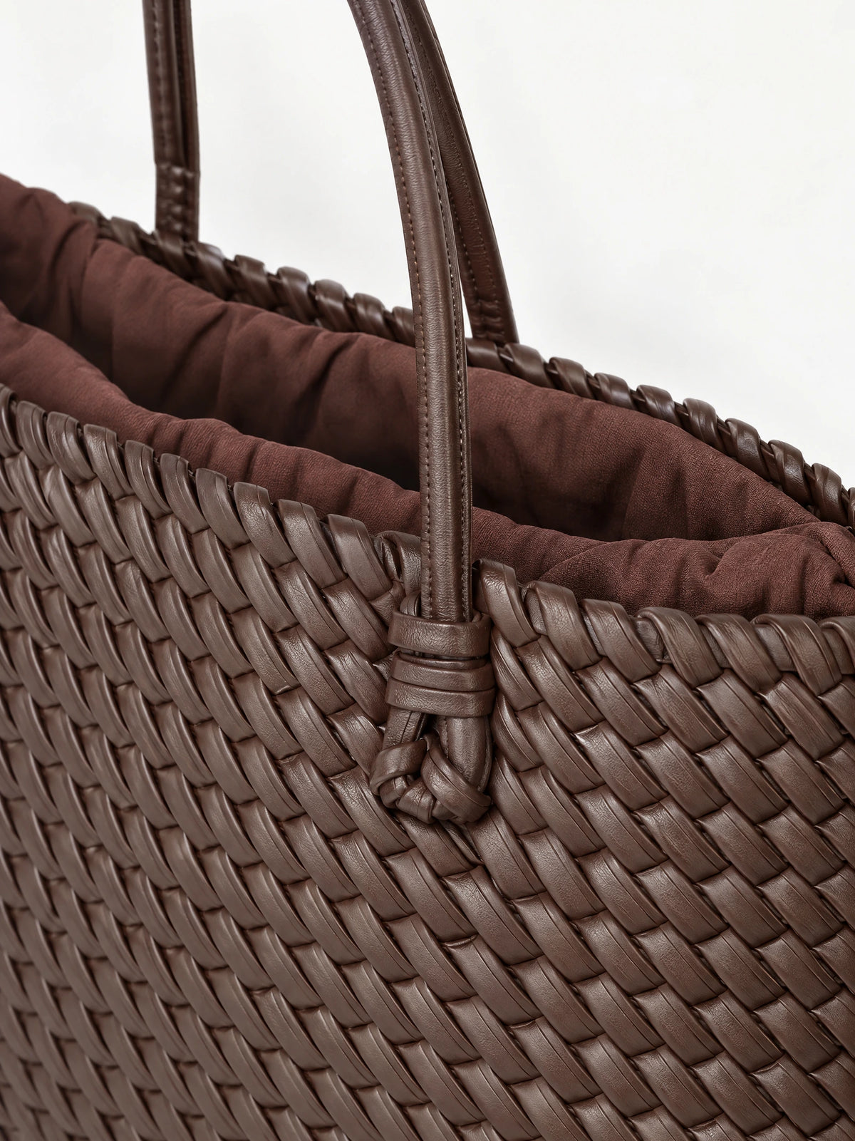 Close-up of the Brown woven shoulder bag showing its braided exterior, knotted handle attachment, and gathered lining.
